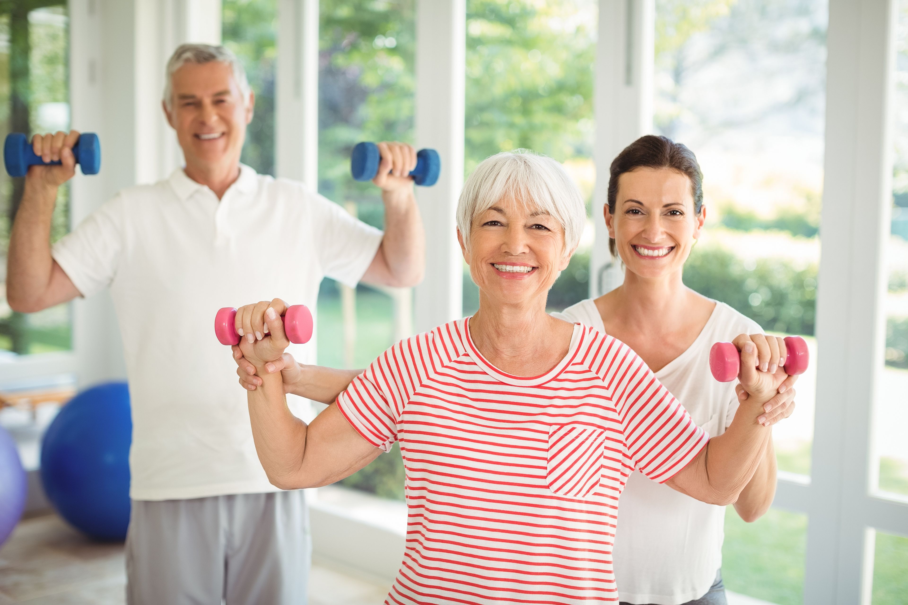 Female trainer assisting senior couple in performing exercise