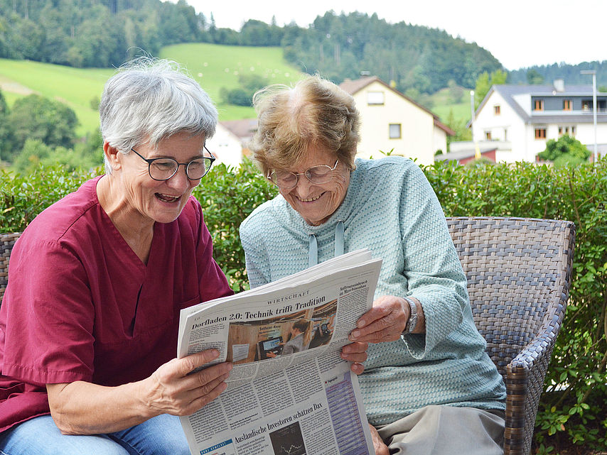 Pflegekraft und Gast lesen zusammen Zeitung