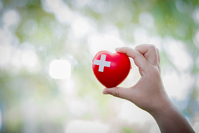 Ein rotes Herz mit einem weißen Kreuz wird in die Höhe gehalten.