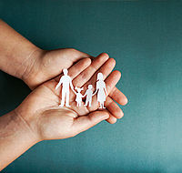 Eine Familie aus Papier gebastelt wird liebevoll in Händen gehalten